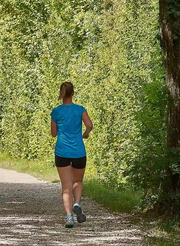 Foto einer Joggerin auf einem Weg besäumt von Bäumen und Büschen, die Schatten werfen.
