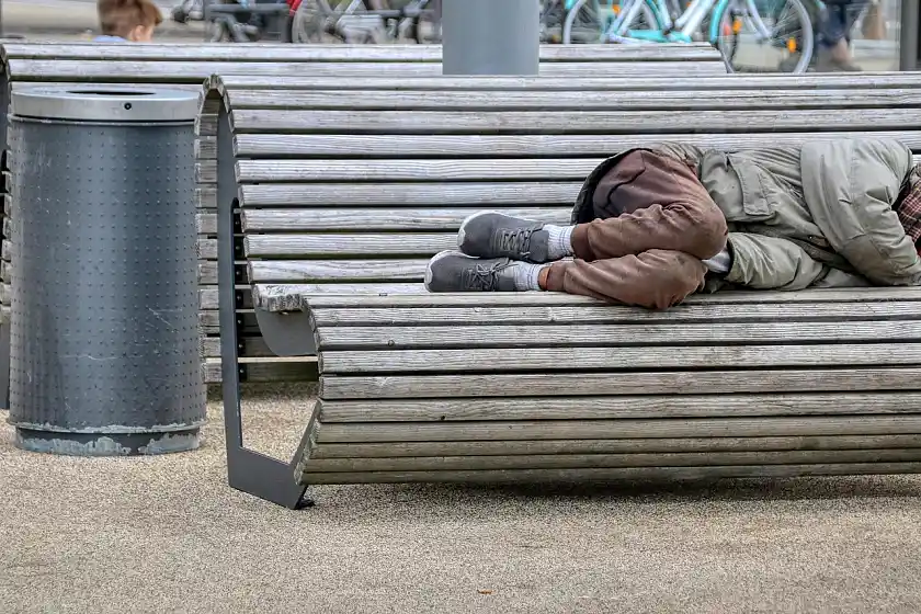 A bench in a city, on which a person is lying. Only the persons shoes and legs are visible.