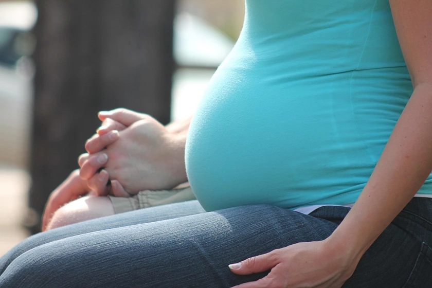 A pregnant woman is seated, wearing a turquoise top. Only her upper body is visible.