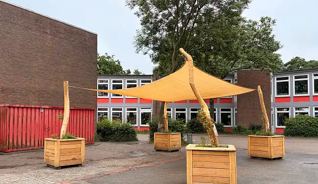 Sonnensegel mit Holzpfählen und bepflanzten Kübeln auf einem Schulhof